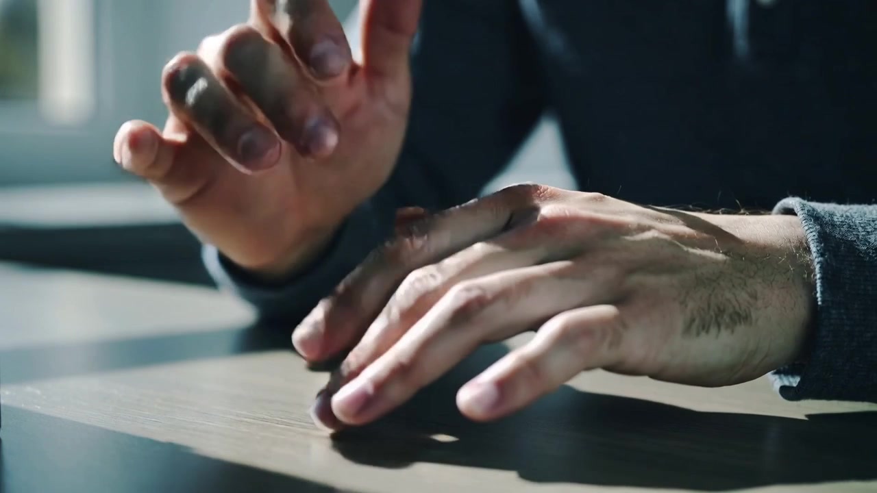 Resting, tapping male hands on wood table by left window, dark sleeve, wrist mark, casting shadows