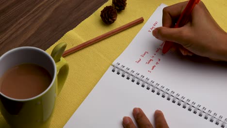 escribiendo un diario con una taza de té usando un bolígrafo rojo fotografía cenital cerca de la mano de una mujer