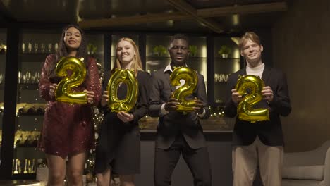 grupo de amigos con ropa elegante sosteniendo globos con los números 2022 mientras bailan en la fiesta de año nuevo