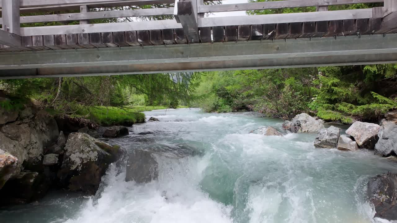 Aerial drone footage gliding over a pristine freshwater stream flowing through the Swiss Alps at Flüelen Pass captures crystal-clear water, rocky alpine terrain, and untouched mountain wilderness