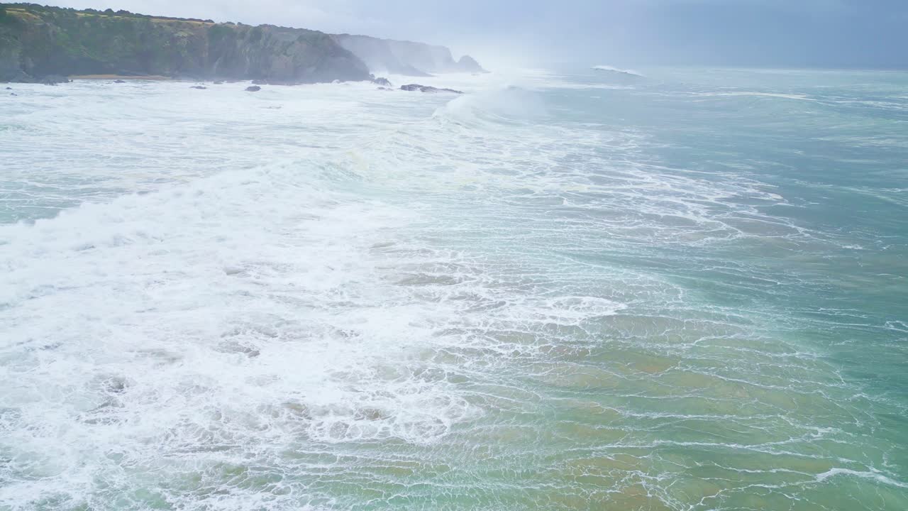 Waves crashing along rocky Aljezur coastline under cloudy skies, calm and powerful vibe