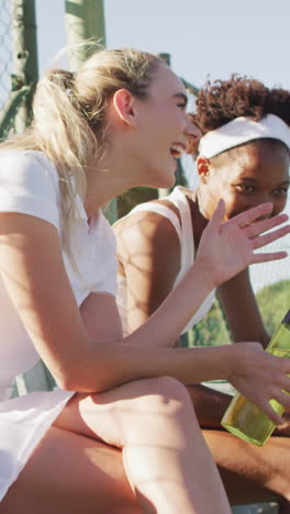 video of happy diverse female tennis players sitting, talking and resting after match