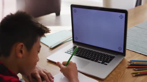 niño asiático en casa, escribiendo durante la lección escolar en línea usando una computadora portátil, con espacio de copia en la pantalla