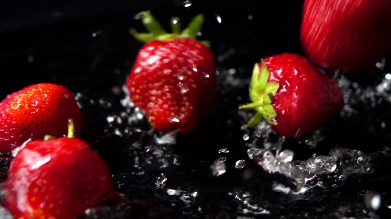 Fragola che cade in acqua su sfondo nero. Rallentatore