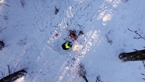 Mann-Sitzt-Auf-Einem-Stuhl-Neben-Einem-Feuer-Und-Einer-Lampe-In-Einem-Schneebedeckten-Wald