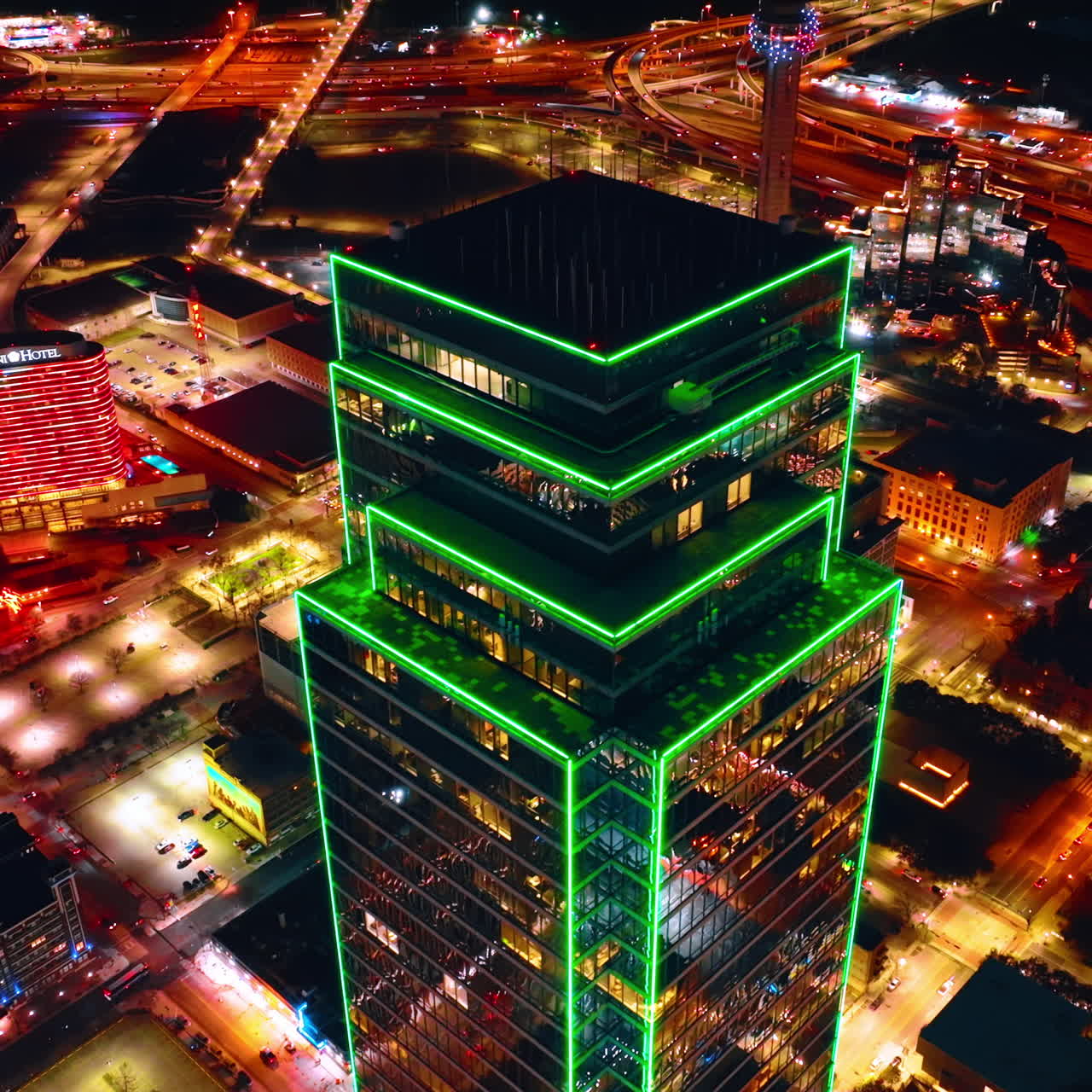 Imagens do topo do Bank of America Plaza com iluminação de argônio verde percorrendo principalmente as bordas e cantos da torre. Vista luminosa de Dallas do alto.