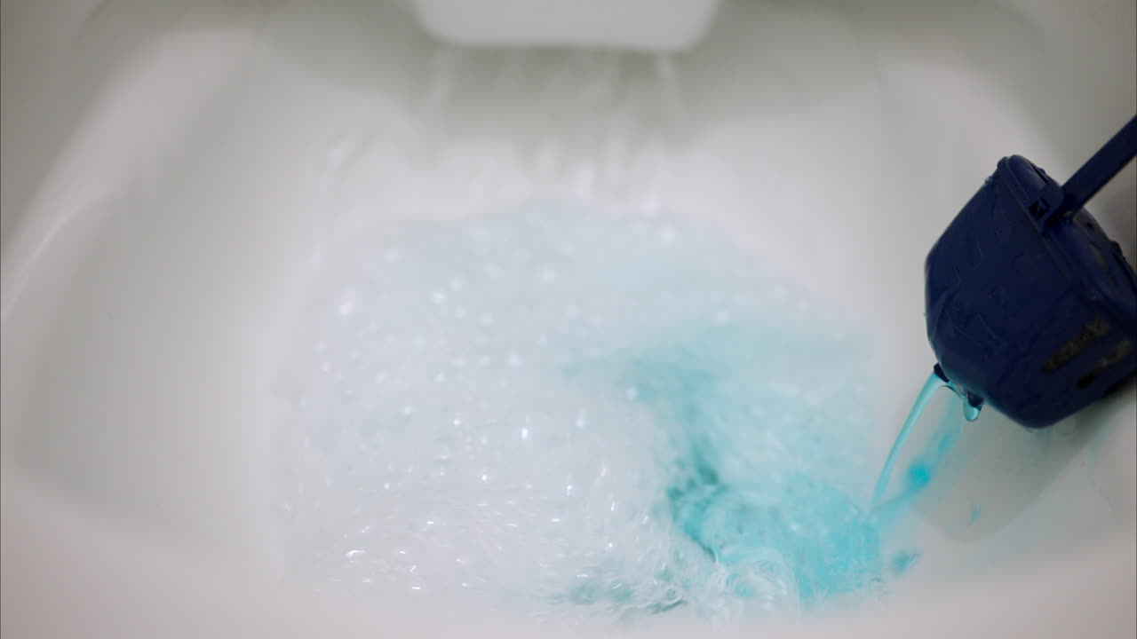 Close up of a toilet bowl flushing with a blue cleaning solution