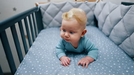 cute baby boy lies in his crib. blue-eyed blond child looking around. close up.