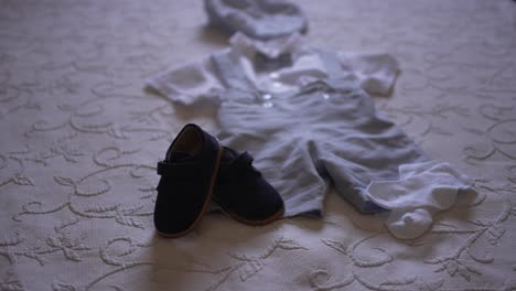 baby boy's outfit, including small shoes, laid out on a bed, ready for a special occasion