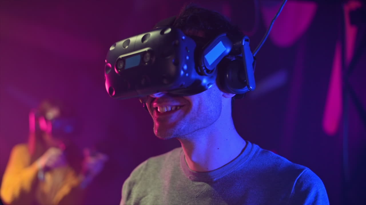 A joyful, shocked man is playing on VR treadmill with helmet. Other people playing nearby. Slow motion