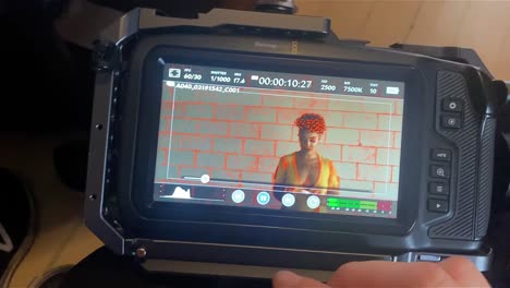 a videographer starts playback on her cinema camera of a woman in a yellow dress with a candle against a white brick wall
