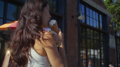la morena disfruta de un postre frío en un paseo por la ciudad. la mujer asiática camina comiendo helado.