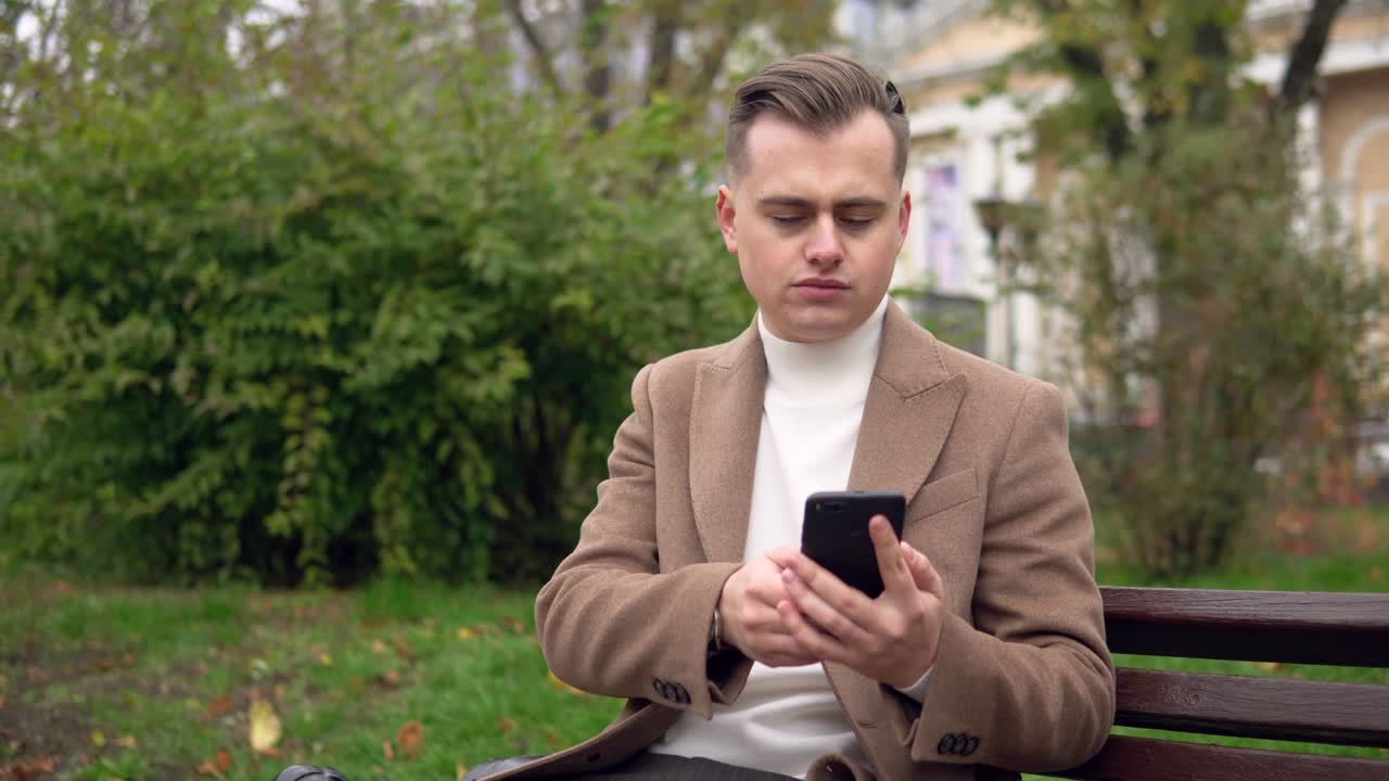 Elegant man uses smartphone while sitting on a bench on the street. Business. Social Networking