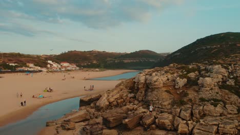 Person,-Die-über-Einen-Felsigen-Gipfel-Hinuntergeht,-Umgeben-Von-Wasser-Auf-Foz-De-Lizandro,-Portugal