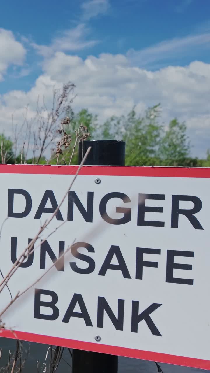 Public safety sign on riverbank reads 'Danger Unsafe Bank' VERTICAL