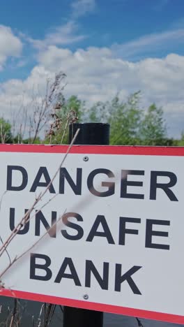 public safety sign on riverbank reads 'danger unsafe bank' vertical
