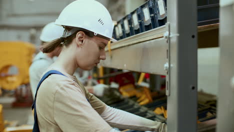 female worker sorting details on shelf in industrial factory