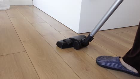 a woman in slippers vacuums a wood floor