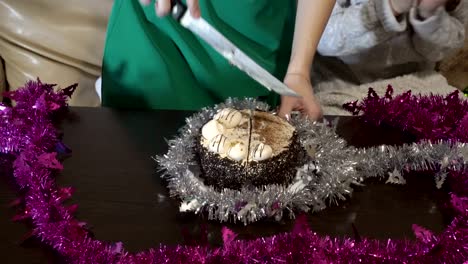 children clap their hands and cut the chocolate cake into pieces with a large knife on the table decorated with tinsel during the holiday home. close up. the view from the top. 4k.