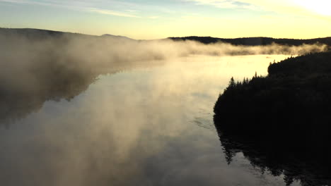 aerial drone shot at sunset of the epic golden mist and calm waters of the spectacle ponds with the dark silhouette of the forest in the maine wilderness