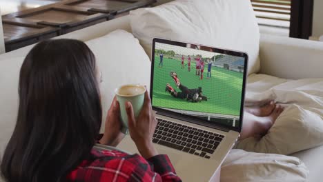 compuesto de una mujer sentada en casa sosteniendo un café viendo un partido de hockey en una computadora portátil