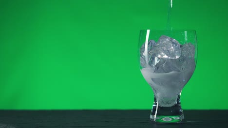 vierte agua con gas en una copa de vidrio con pedazos de hielo, sobre un fondo de clave de croma.