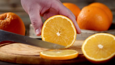 hand of man with knife cut ripe orange into round slices.