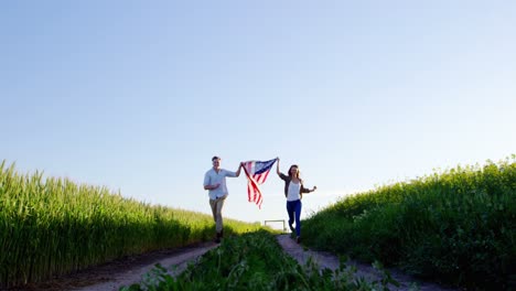 Couple-holding-american-flag-and-running-in-field