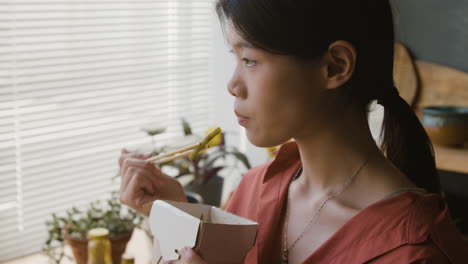 young woman enjoying delicious takeout meal with chopsticks