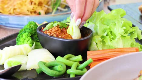 손으로 채소를 매운 태국 소스에 담아 넣는 것