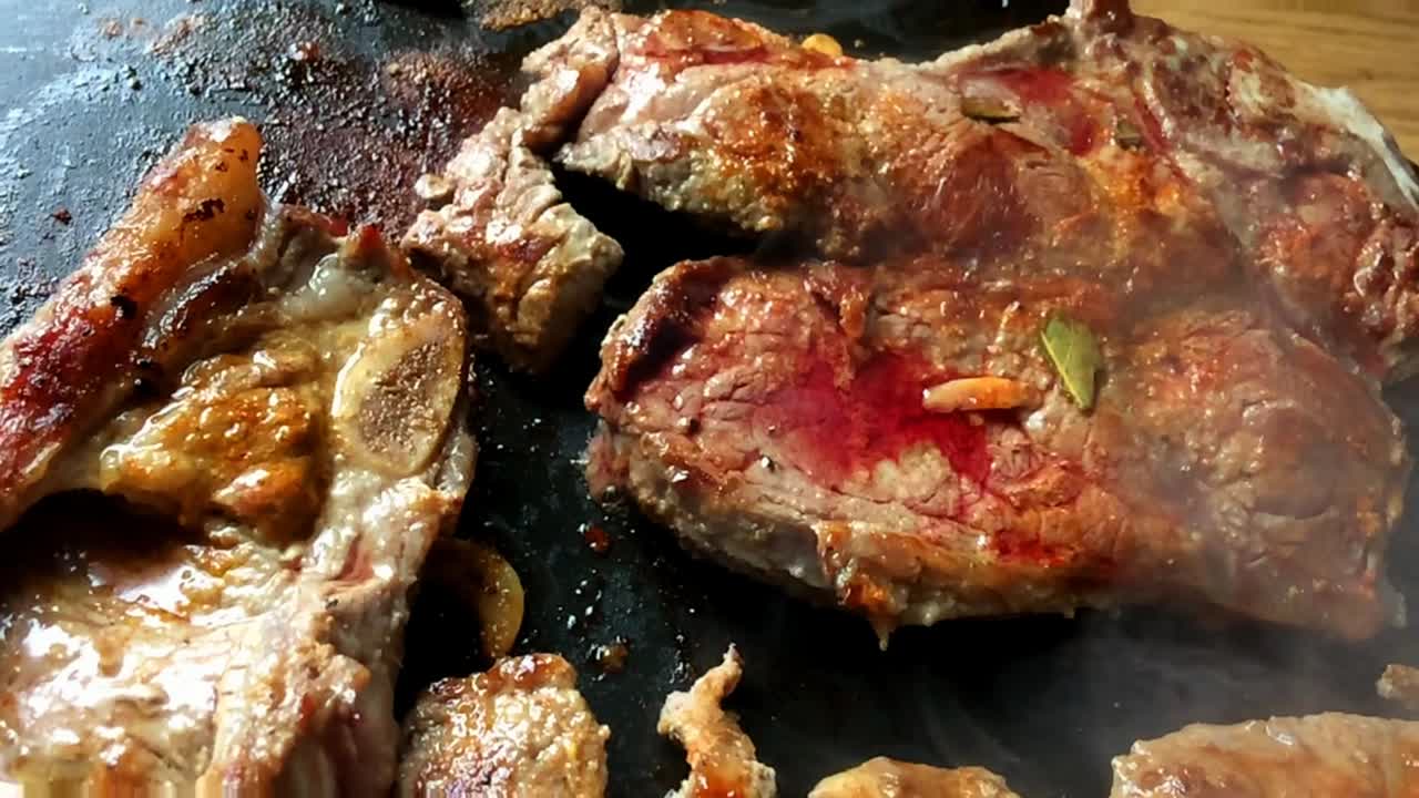 Fresh cow chops beef steaks grilled seasoned on round electric griddle slow-motion zoom alternative green cooking kitchen appliances healthy meal cusine garlic herbs spices delicious electricity