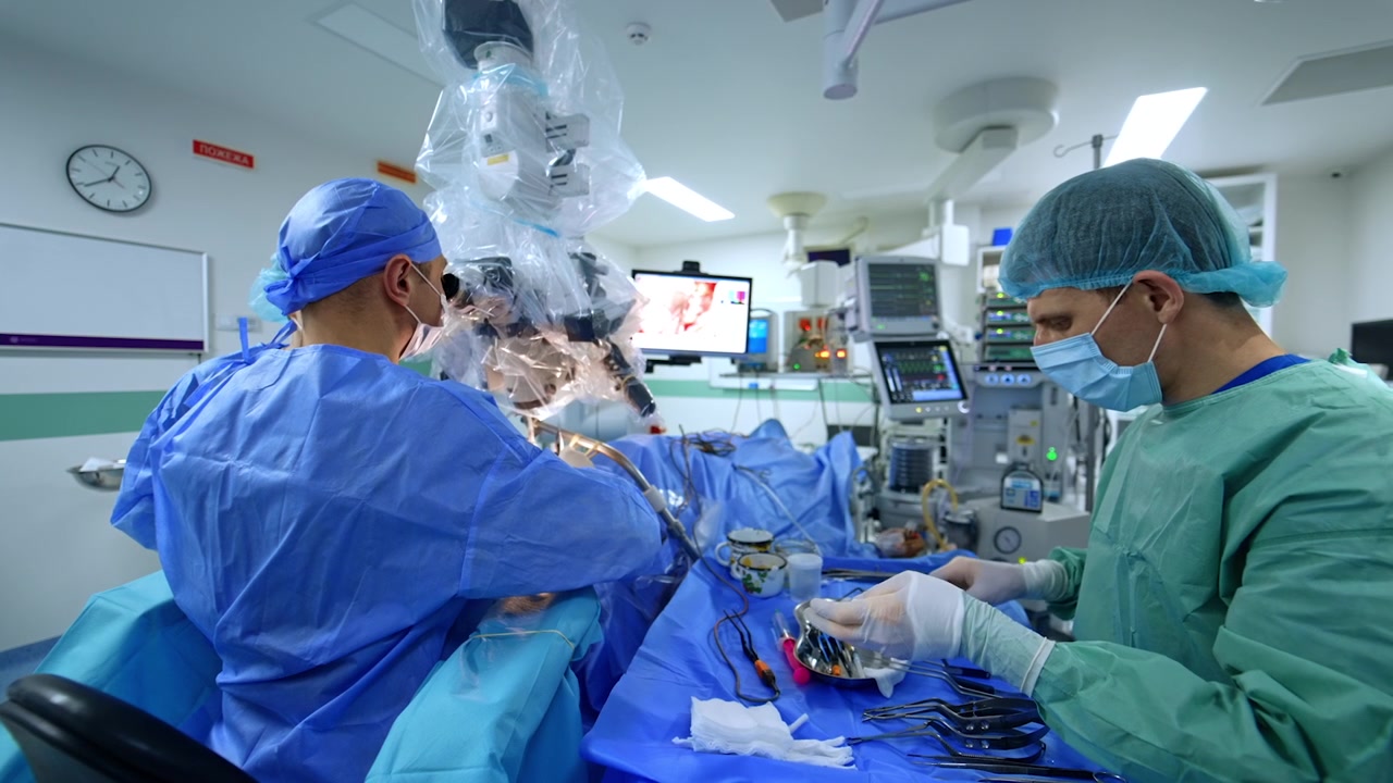 Kyiv, Ukraine, 5 May 2026: Neurosurgeons working under surgical microscope with instrument table. Surgeon leans into eyepiece, assistant hands tools, sterile tray with instruments spread out.