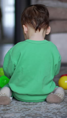 little child sitting his back to camera plays with toys. baby turns and approaches camera crawling. black cat sitting beside. vertical video