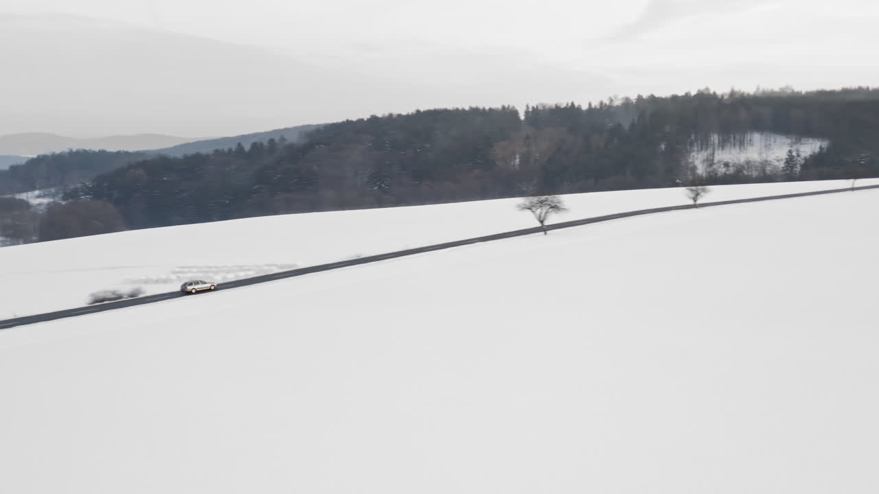 눈으로 뒤덮인 산을 가로질러 운전하는 자동차의 공중 추적 샷, 겨울 장면