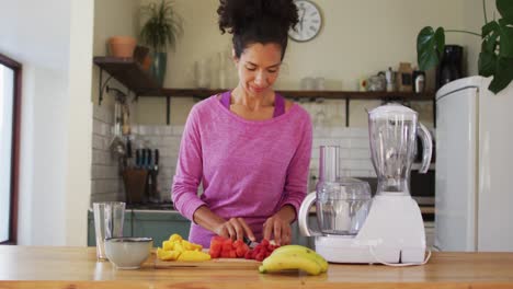 mujer de raza mixta cortando frutas para hacer jugo de frutas en la cocina en casa