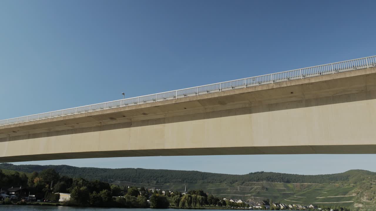 Crossing under a huge bridge over the river Mosel. Tracking shot from a boat with camera tilting up.