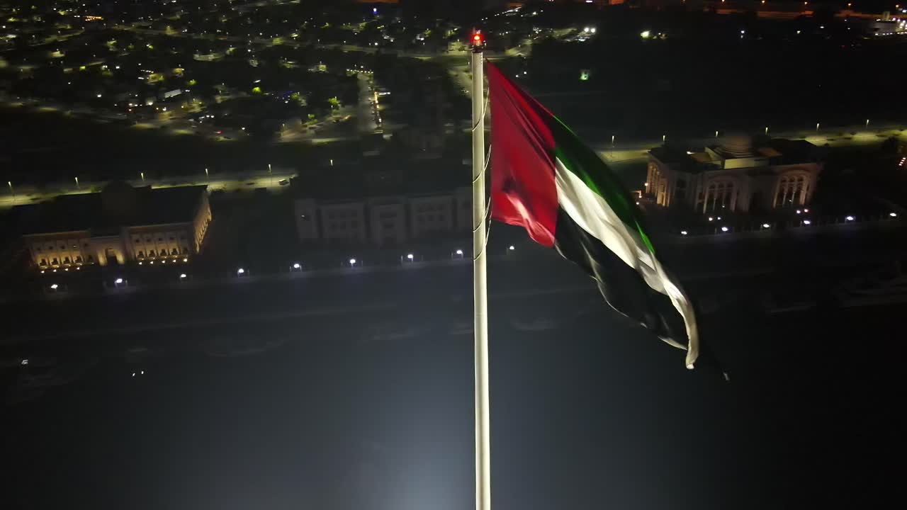 4k: vista aérea nocturna de la bandera de los emiratos árabes unidos ondeando en el aire, el símbolo nacional de los emiratos árabes unidos