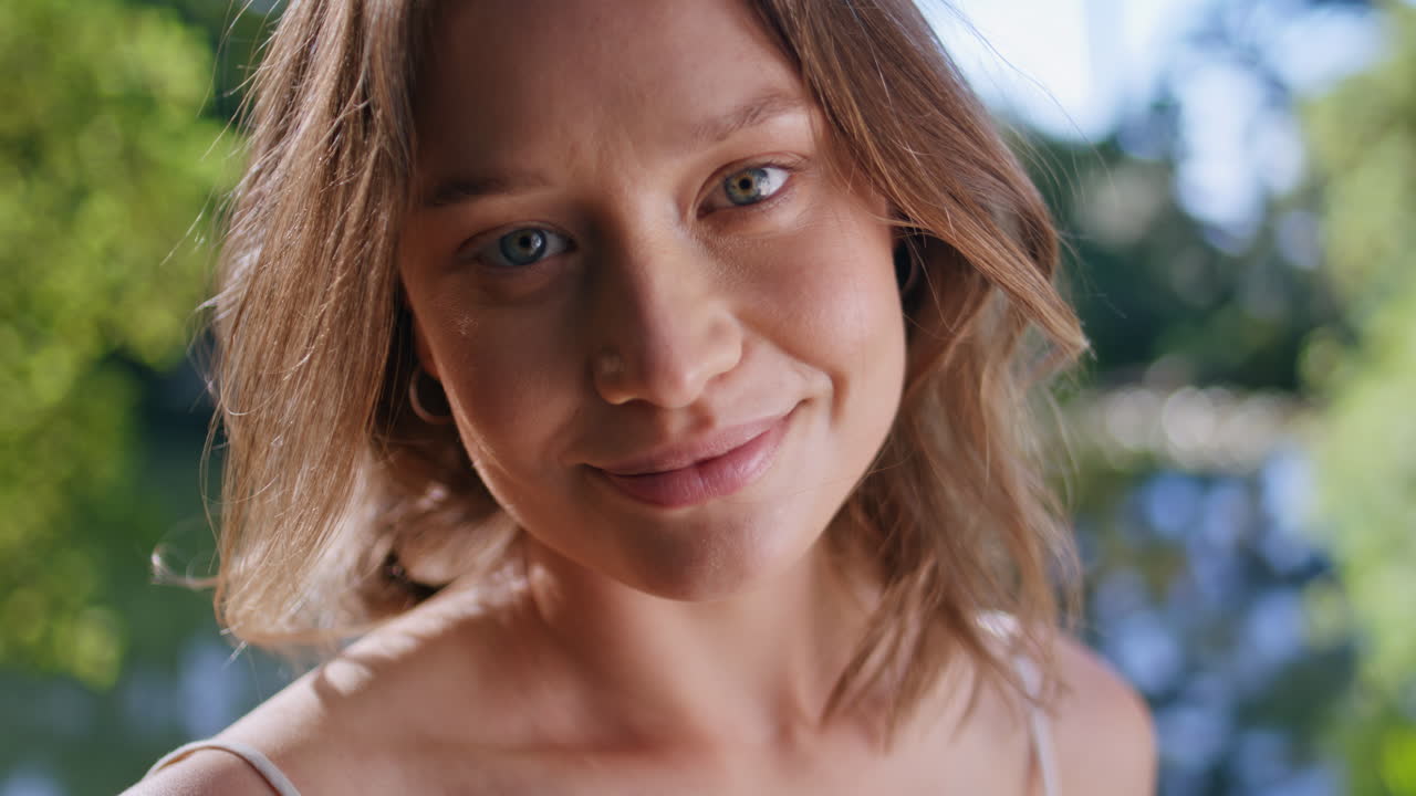 Modella sorridente che guarda la fotocamera in primo piano in un parco. Ritratto di ragazza felice immersa nel verde