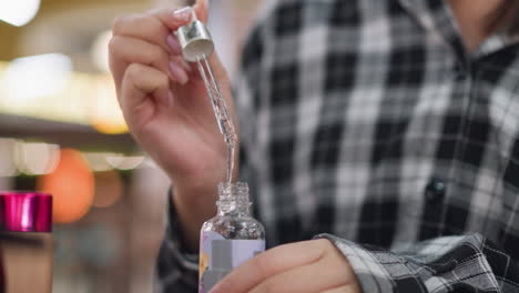 closeup partial view of young girl holding serum dropper, observing liquid dripping into bottle, her neatly manicured hands carefully handle skincare product in a serene, stylish beauty