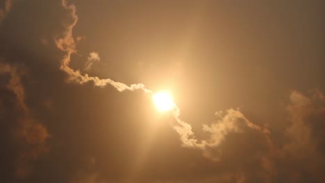 low angle view of glimmering sun peeking up through gigantic slowly moving cloud with vast orange sky