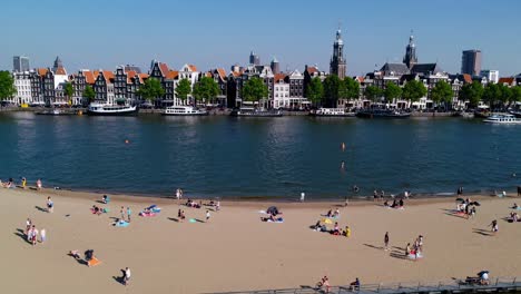 aerial view of people sunbathing and swimming on the beach along amstel river in amsterdam, netherlands, enjoying a sunny summer day with the cityscape in the background