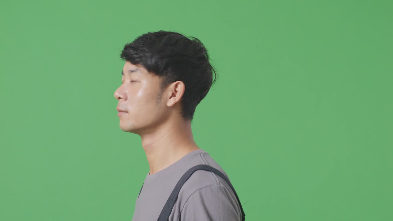 녹색 스크린 배경 스튜디오에서 걸어다니고 둘러보는 아시아 남성 노동자의 측면 뷰 클로즈업