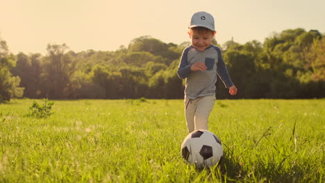 the boy runs with a soccer ball laughing at the sunset in slow motion.