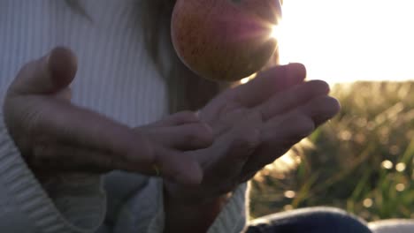 Woman-throwing-juicy-red-apple-against-sunlit-background