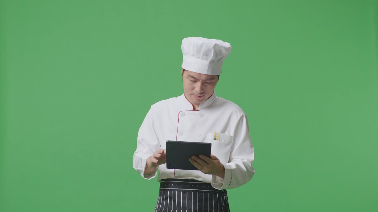 Asian Man Chef Using A Tablet While Standing In The Green Screen Background Studio