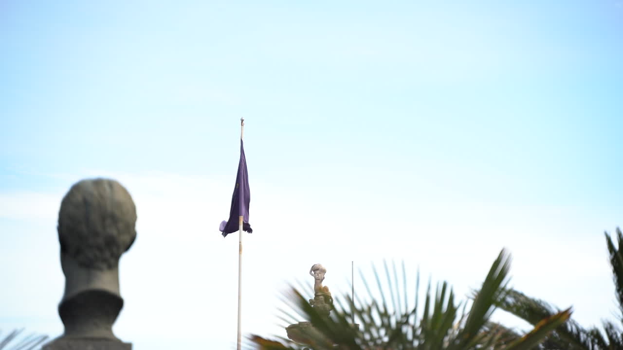 Parco con statue e bandiera dell'Unione Europea che sventola al vento, ripresa in movimento