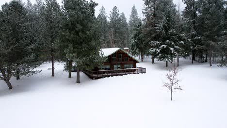 Aerial-log-cabin-in-the-woods-during-winter-with-lots-of-snow-and-trees