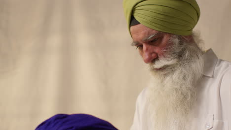 Fotografía-De-Estudio-De-Dos-Hombres-Sikh-Atando-Tela-Para-Un-Turbante-Contra-Un-Fondo-Liso