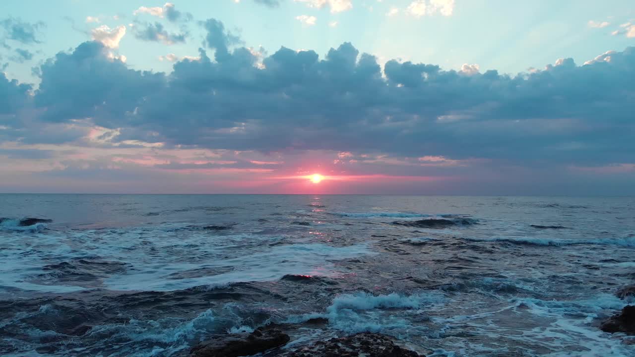 Aerial shot flying close to the sea and the rocky shore on a beautiful cloudy sunrise