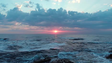 aerial shot flying close to the sea and the rocky shore on a beautiful cloudy sunrise